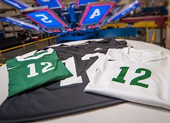 Green and white number 12 football jerseys laid out under a screen printing press