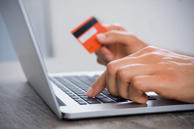 Hands typing on a laptop keyboard while holding an orange credit card