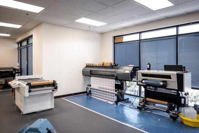 Silverscreen's digital print room, with wide-format printers and a heat press in front of tall office windows