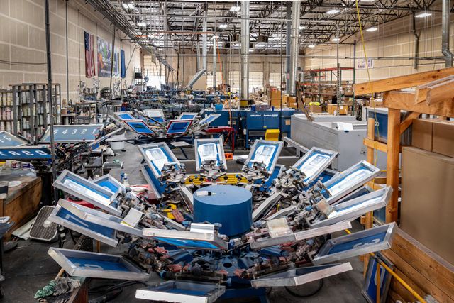 Close-up of an automatic carousel screen printing press loaded with screens, with more presses lined up behind it