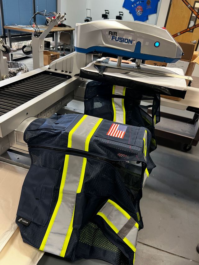 Navy safety vest with reflective stripes and an American flag patch on a heat press