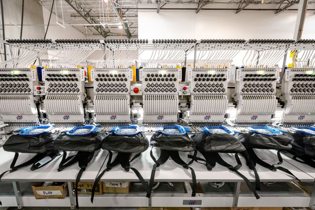 Row of multi-head embroidery machines stitching black backpacks